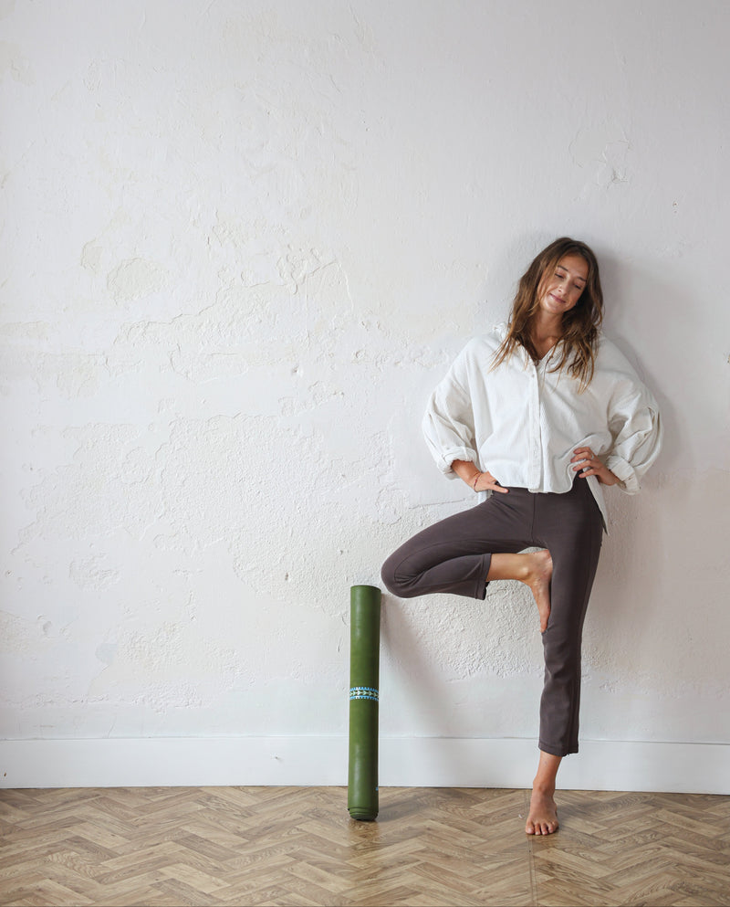 Woman standing with one leg on a yoga bolster against a white wall