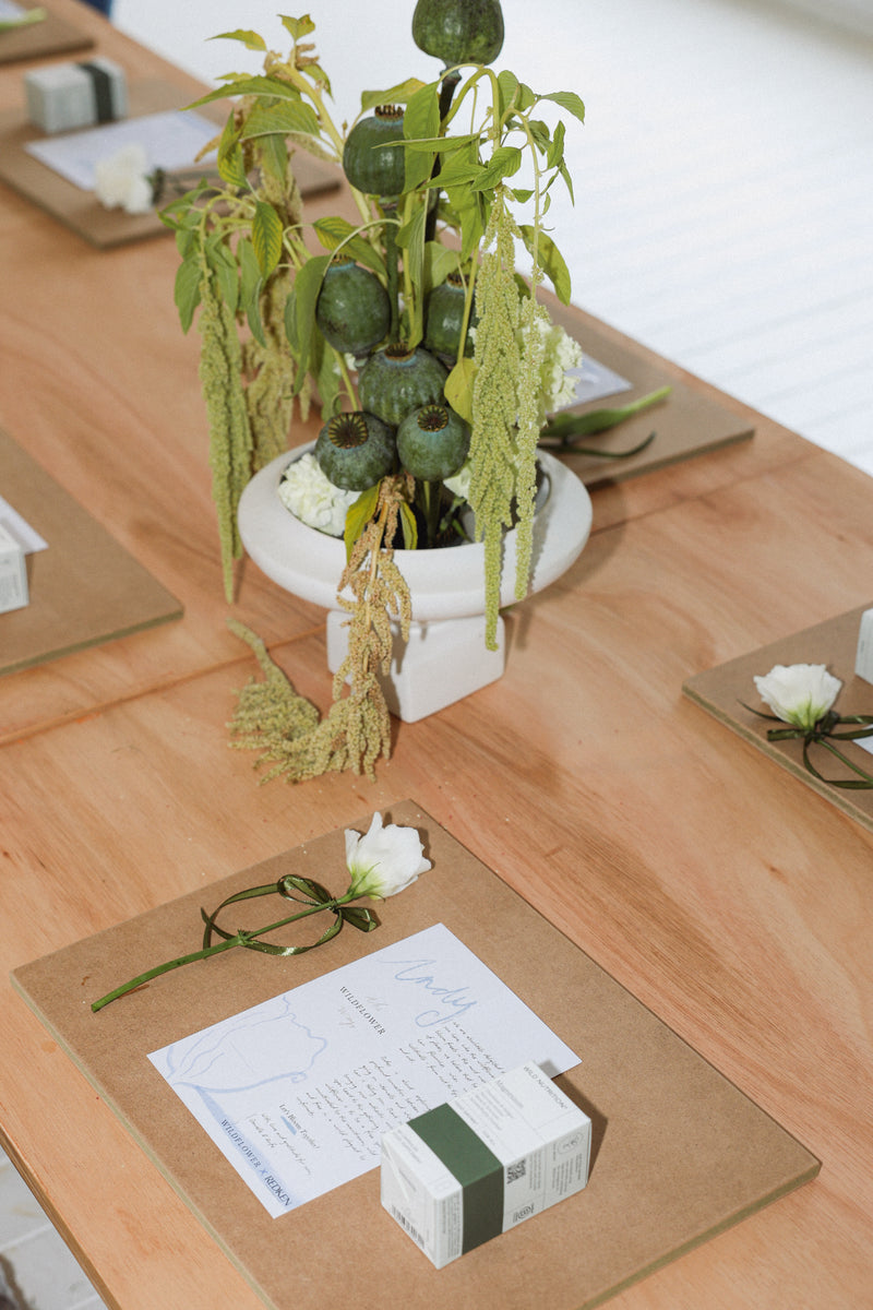 Decorative table setting with plants, white flowers, and stationery on a wooden surface.