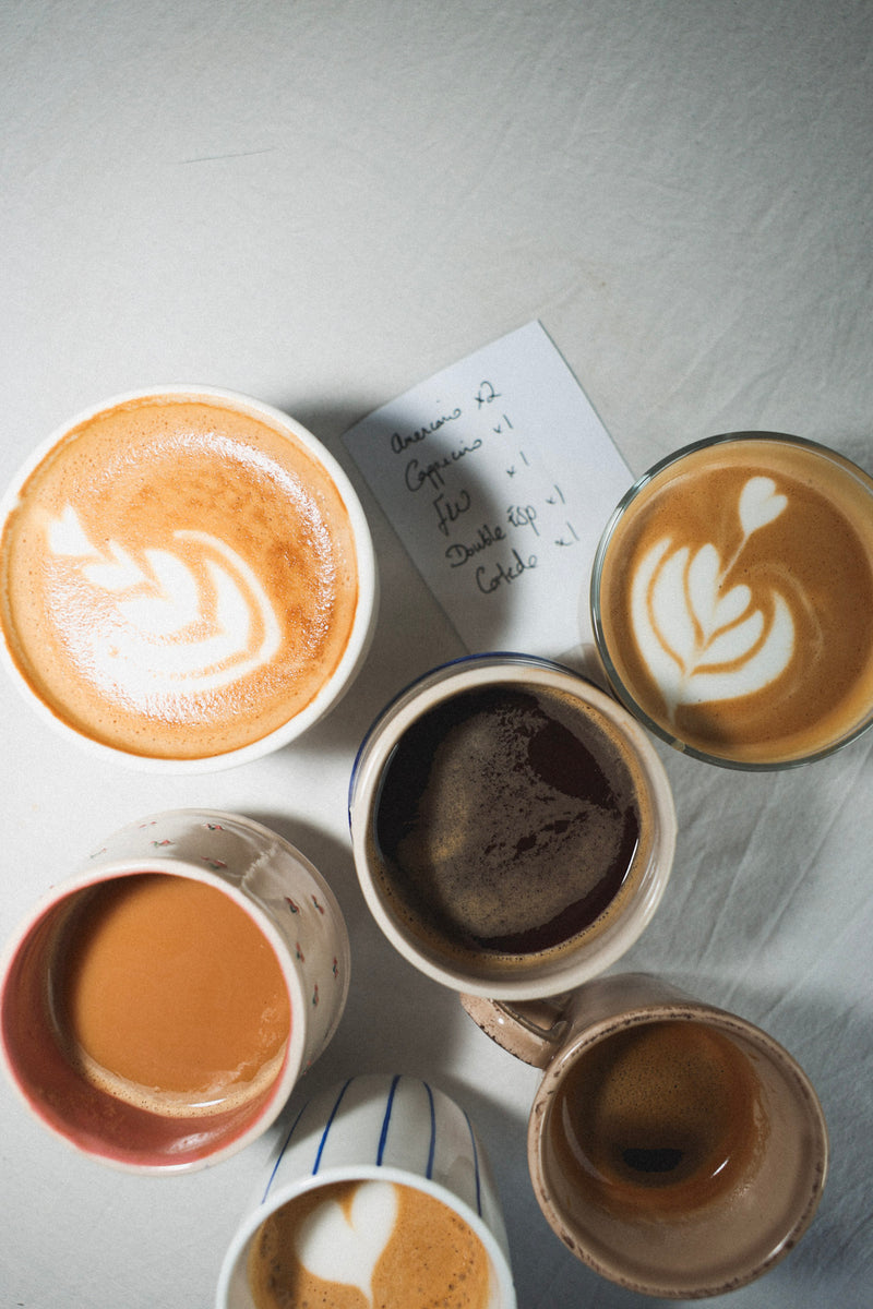 Collection of coffee cups with different types of coffee and latte art on a light surface.