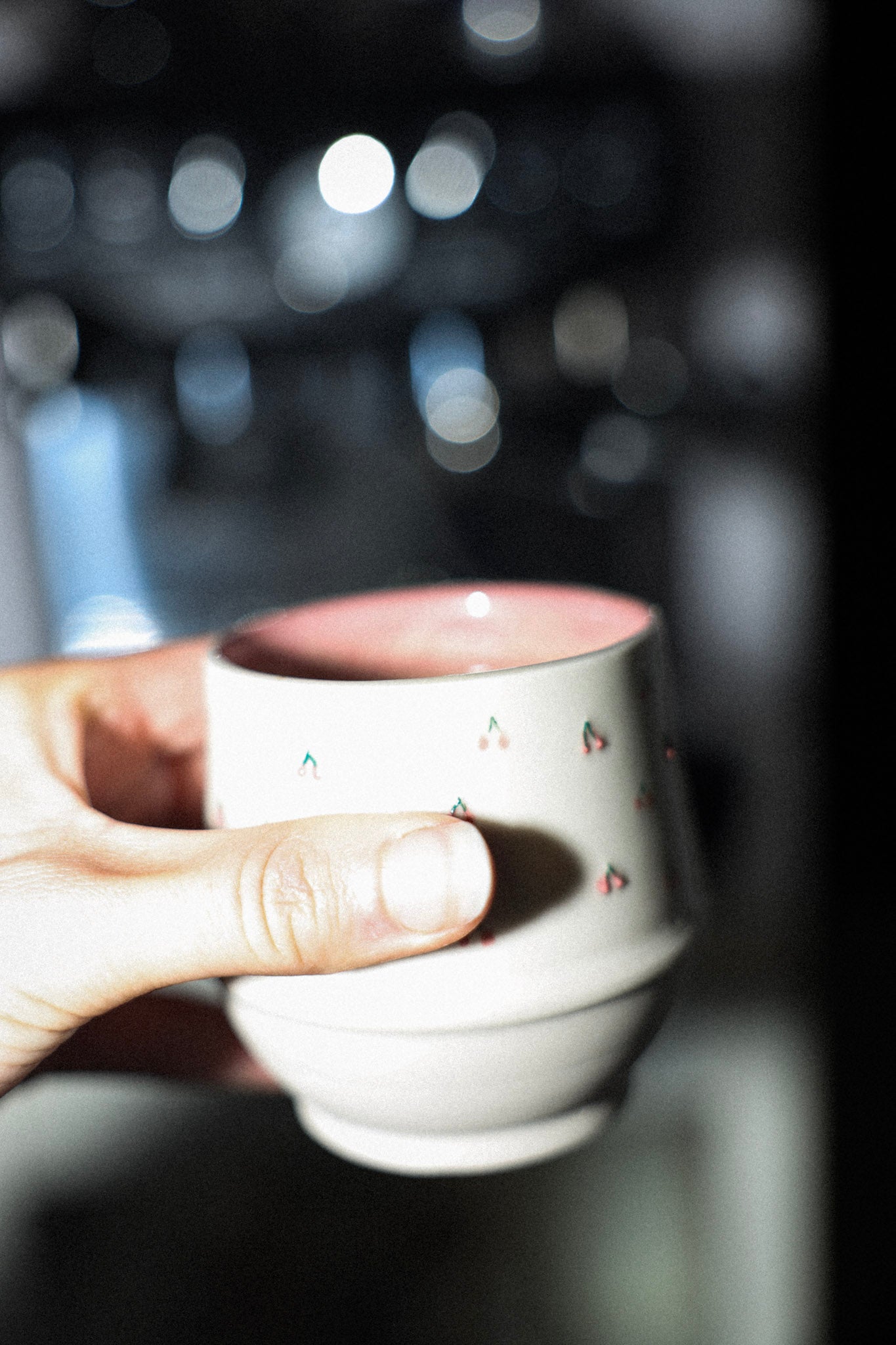 Hand holding a small white ceramic cup with a blurred background