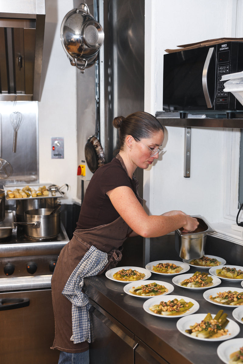 Woman in a kitchen preparing food on a counter with multiple plates of food.