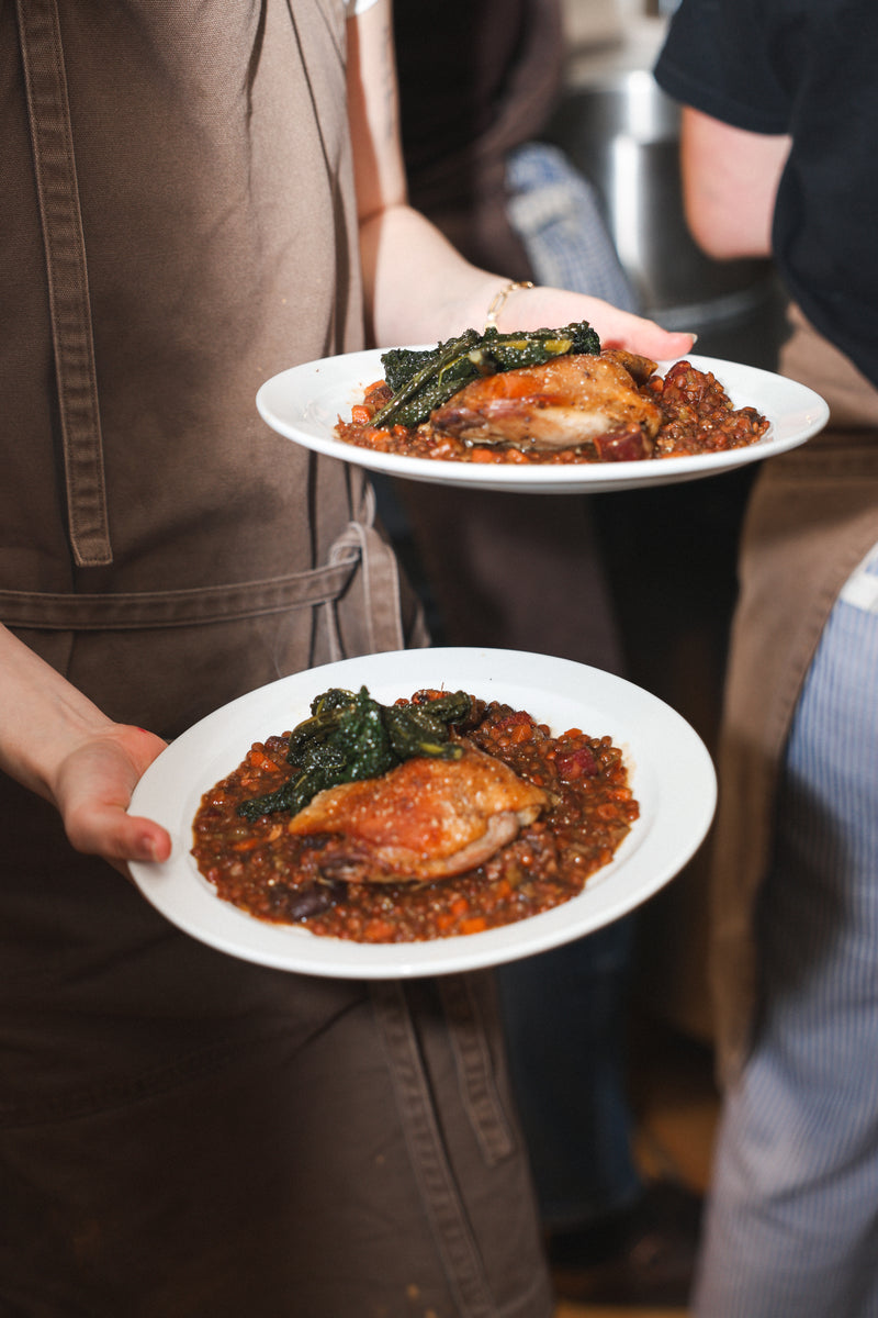 Two plates of food being held by a person in a brown apron.