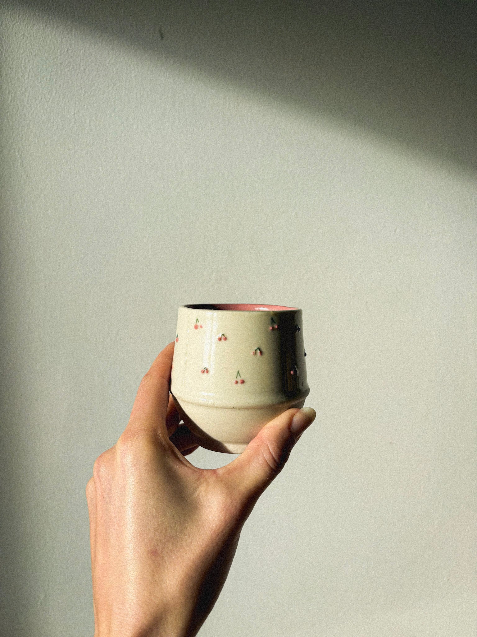 Hand holding a small ceramic cup with a plain background