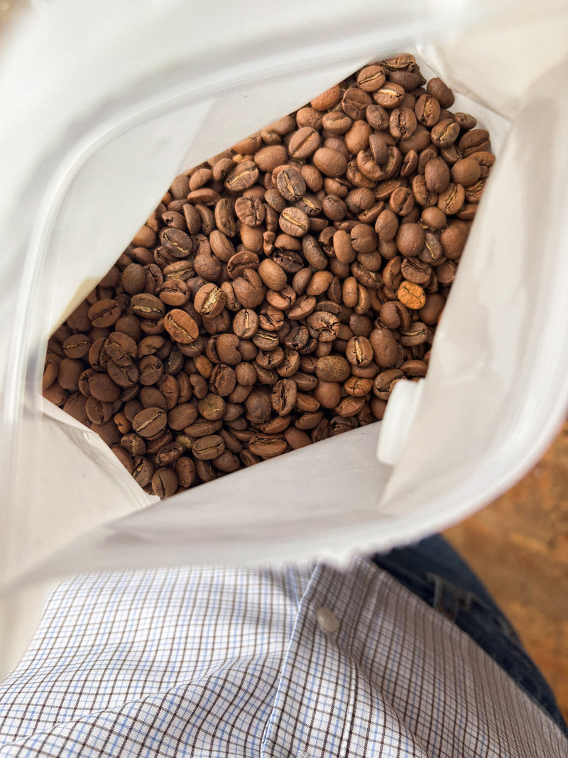Bag of coffee beans held by a person wearing a checkered shirt.